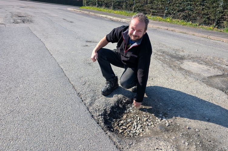 Cllr Andy Coppin pictured with a particularly large pothole on the entrance to Home Bargains in Bodmin (Picture: Aaron Greenaway/Tindle)